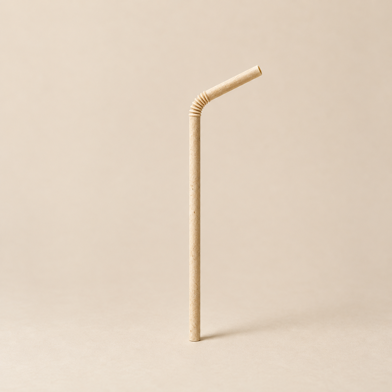 One natural tan agave-fiber straw with a gently bent flexible neck on a warm beige background