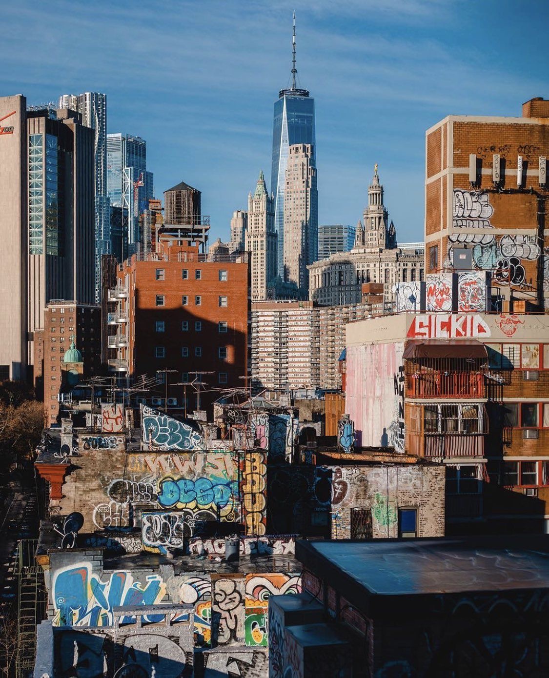 Colorful graffiti-covered rooftops with One World Trade Center against a blue sky
